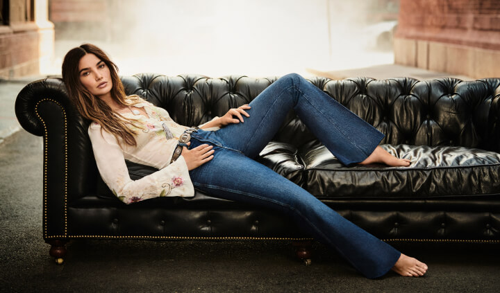 Model laying on couch wearing embroidered top and Sasson denim