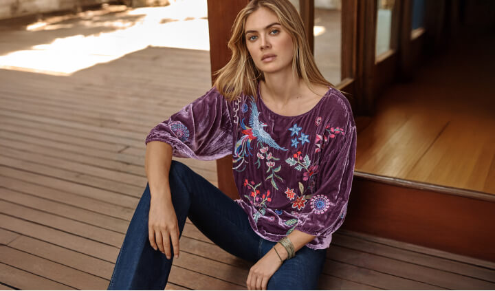 Model wearing a sugarplum purple embroidered boatneck blouse and jeans